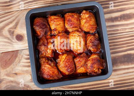 Gebratene Hähnchenschenkel auf Backblech. Gekochte gebackene Hühnerteile liegen auf einem Holztisch. Nahaufnahme. Draufsicht Stockfoto