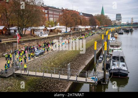 Bremen, Deutschland. 24th. November 2021. An der Weserpromenade zwischen Bürgermeister-Smidt-Brücke und Wilhelm-Kaisen-Brücke demonstrieren die Beschäftigten des öffentlichen Dienstes mit einer Menschenkette. Im anhaltenden Tarifkonflikt für die Beschäftigten der Bundesländer setzt die Gewerkschaft Verdi ihre Warnstreiks fort. Verdi und der Beamtenverband dbb fordern bundesweit fünf Prozent mehr Lohn für die mehr als eine Million Staatsangestellte, mindestens aber 150 Euro mehr pro Monat und sogar 300 Euro mehr im Gesundheitswesen. Quelle: Sina Schuldt/dpa/Alamy Live News Stockfoto