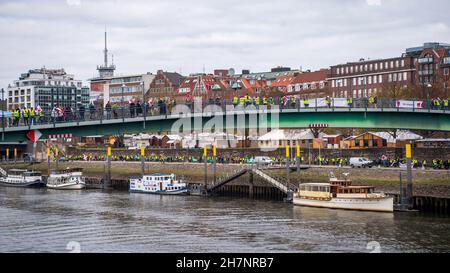 Bremen, Deutschland. 24th. November 2021. An der Weserpromenade zwischen Bürgermeister-Smidt-Brücke und Wilhelm-Kaisen-Brücke demonstrieren die Beschäftigten des öffentlichen Dienstes mit einer Menschenkette. Im anhaltenden Tarifkonflikt für die Beschäftigten der Bundesländer setzt die Gewerkschaft Verdi ihre Warnstreiks fort. Verdi und der Beamtenverband dbb fordern bundesweit fünf Prozent mehr Lohn für die mehr als eine Million Staatsangestellte, mindestens aber 150 Euro pro Monat und sogar 300 Euro mehr im Gesundheitswesen. Quelle: Sina Schuldt/dpa/Alamy Live News Stockfoto