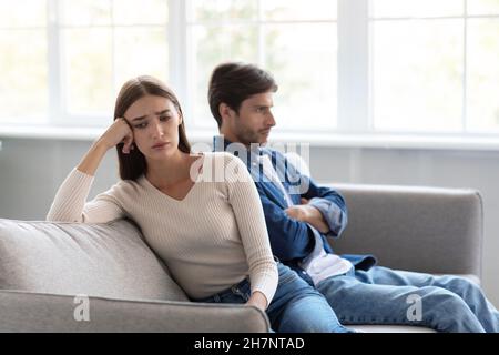 Traurig depressive junge kaukasische Frau ignoriert unglücklichen Ehemann, der im Wohnzimmer auf dem Sofa sitzt Stockfoto