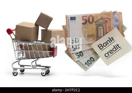Pakete in einem kleinen Einkaufswagen und Bargeld sowie Notiz mit Aufschrift Bankkredit als Konzept von Schulden und Verschuldung isoliert auf weißem Bac Stockfoto