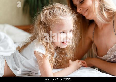 Porträt von Tochter und Mutter verbringen den Morgen zusammen zu Hause. Schönes Kind Mädchen kaukasischen Kind mit Mutter im Bett. Liebevolle, fürsorgliche Mutter lässt das Kind aufwachen Stockfoto