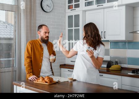 Junges Paar streitet mit Kampf, brüllt in Küche Hause Interieur. Frau Mann haben Skandal streiten Streit während des Frühstücks Telefongespräch Stockfoto