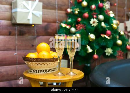 Zwei Gläser Champagner mit einem Korb voller leuchtend reifer Orangen auf dem Hintergrund eines geschmückten Weihnachtsbaums, das Konzept eines Neujahrsabends. Stockfoto