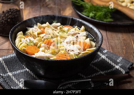 Dampfaufsatz mit Hühnernudelsuppe mit Karotten und Dill auf einem rustikalen Holztisch Stockfoto