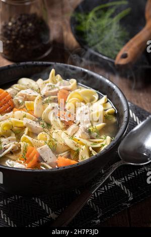 Dampfaufsatz mit Hühnernudelsuppe mit Karotten und Dill auf einem rustikalen Holztisch Stockfoto