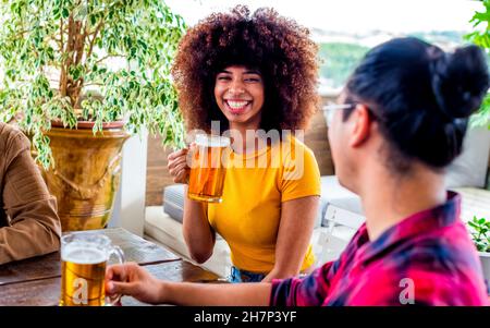 Ein paar Freunde Porträt Bier trinken auf Happy Hour Feier Urlaub sitzen auf einem Tisch Spaß zusammen. Multiethnische lockige Frau Stockfoto