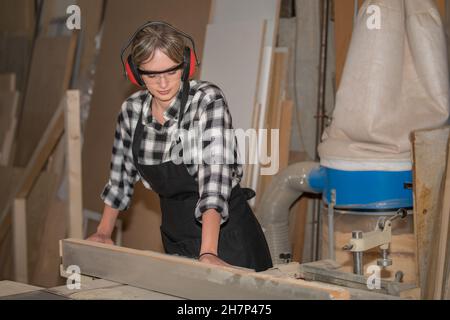 Junge Frau als Zimmermann mit Schutzbrille und Gehör Schutz funktioniert auf Hobelmaschine Stockfoto