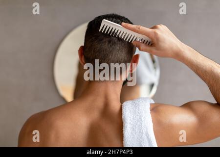 Rückansicht eines jungen Mannes, der im Spiegel sah und Haare putzte Stockfoto