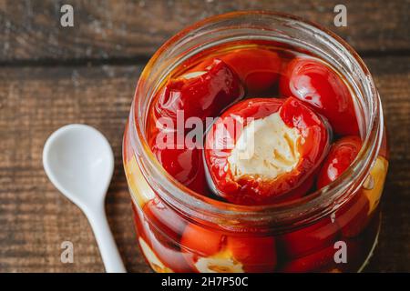 Gefüllte Kirschpaprika mit Ricotta-Käsefüllung im Glas auf Holzboden Stockfoto