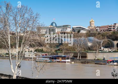 Blick vom Fluss Kura auf das rohrförmige Ausstellungszentrum und das Musiktheater, den Präsidentenpalast und die Kathedrale von Sameba. Tiflis, Georgien. Stockfoto