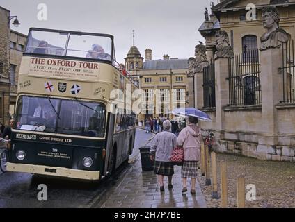 Zwei ältere Frauen mit Regenschirm und einem Touristenbus an einem regnerischen Tag in einer breiten Straße im Zentrum von Oxford, Großbritannien Stockfoto