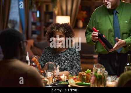 Afrikanische junge Frau, die mit ihren Freunden spricht und lächelt, während sie während einer Party am Tisch zu Abend gegessen hat Stockfoto