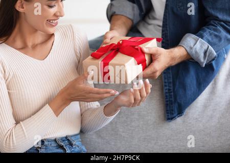 Ein kurzer glücklicher Tausendjähriger Kaukasianer gibt der Dame im Wohnzimmer eine Schachtel Stockfoto