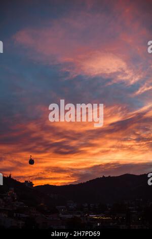 Seilbahn in den Bergen vor dem Hintergrund eines scharlachroten Sonnenuntergangs. Landschaftlich schöner Blick auf den Sonnenuntergang in der Bergstadt. Stockfoto
