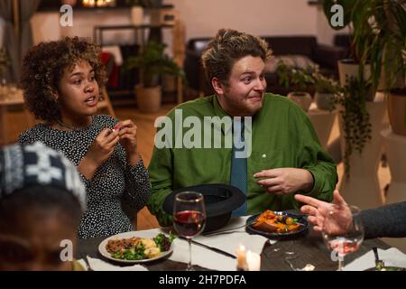 Ein multiethnisches Paar, das während des Treffens auf der Dinner Party mit seinen Freunden spricht Stockfoto