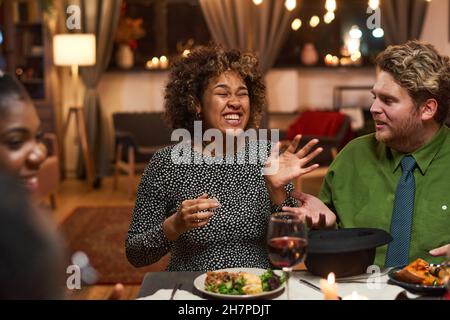 Afrikanische junge Frau lacht, während sie mit ihren Freunden am Esstisch sitzt Stockfoto