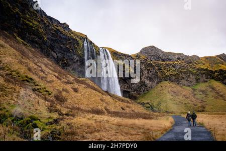 Touristen stehen vor Seljalandsfoss, einem der bekanntesten Wasserfälle im Süden Islands, dem berühmtesten isländischen Wasserfall Stockfoto