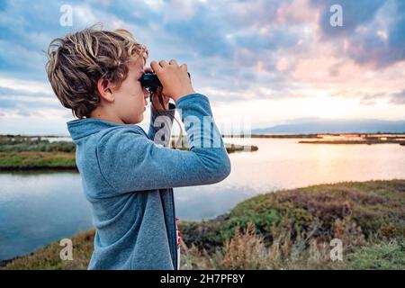 Ein abenteuerlicher Junge erkundet die Landschaft mit einem Fernglas mit dem wolkigen Horizont, dem Konzept, mit Unabhängigkeit und Zukunft aufzuwachsen. Stockfoto