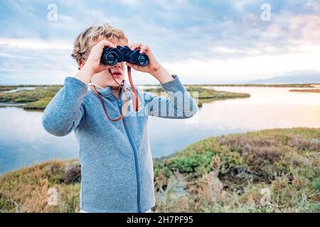 Ein abenteuerlicher Junge erkundet die Landschaft mit einem Fernglas mit dem wolkigen Horizont, dem Konzept, mit Unabhängigkeit und Zukunft aufzuwachsen. Stockfoto