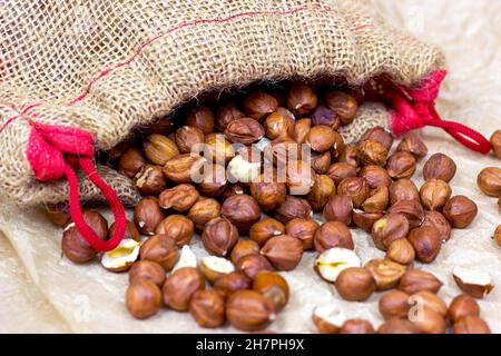 Geschälte braune Haselnüsse gießen aus dem Stoffbeutel auf hellem Hintergrund. Stockfoto