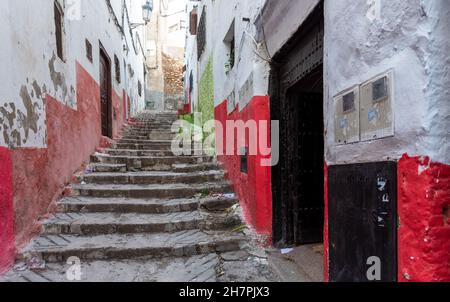 In der Medina von Tetouan in Marokko. Eine alte Treppe klettert eine Gasse zwischen den Wänden hinauf, die in hellen Farben, rot und grün, gemalt sind Stockfoto