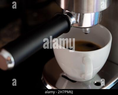 Nahaufnahme eines Kaffees, der aus einer Kaffeemaschine in eine weiße Keramikschale gegossen wird Stockfoto