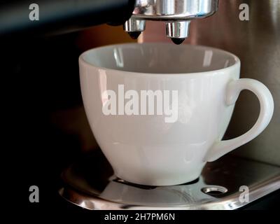 Nahaufnahme eines Kaffees, der aus einer Kaffeemaschine in eine weiße Keramikschale gegossen wird Stockfoto