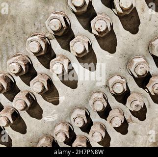 Aus dem Licht und den Schatten einer Reihe von Muttern und Schrauben auf einer Verstärkungsplatte, die einen Metallträger in Position hält, entsteht ein Muster. Stockfoto