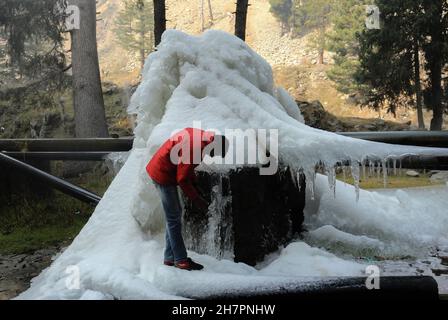 Srinagar, Indien. 24th. November 2021. Ein Kashmiri-Mann geht an Eiszapfen vorbei, die durch Wasser aus einer Trinkwasserleitung bei Tangmarg, etwa 50 Kilometer nördlich von Srinagar City, entstehen. Eine kalte Welle verstärkte ihren Griff auf Jammu und Kaschmir weiter, wobei die meisten Orte im Bundesstaat Temperaturen unter dem Nullpunkt aufzeichneten. Die Temperaturen unter dem Gefrierpunkt haben viele Gewässer in Kaschmir gefroren und sogar Trinkwasserhähne sind an einigen Stellen gefroren. Kredit: Majority World CIC/Alamy Live Nachrichten Stockfoto