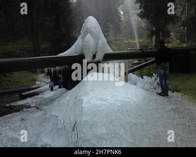 Srinagar, Indien. 24th. November 2021. Ein Kashmiri-Mann geht an Eiszapfen vorbei, die durch Wasser aus einer Trinkwasserleitung bei Tangmarg, etwa 50 Kilometer nördlich von Srinagar City, entstehen. Eine kalte Welle verstärkte ihren Griff auf Jammu und Kaschmir weiter, wobei die meisten Orte im Bundesstaat Temperaturen unter dem Nullpunkt aufzeichneten. Die Temperaturen unter dem Gefrierpunkt haben viele Gewässer in Kaschmir gefroren und sogar Trinkwasserhähne sind an einigen Stellen gefroren. Kredit: Majority World CIC/Alamy Live Nachrichten Stockfoto