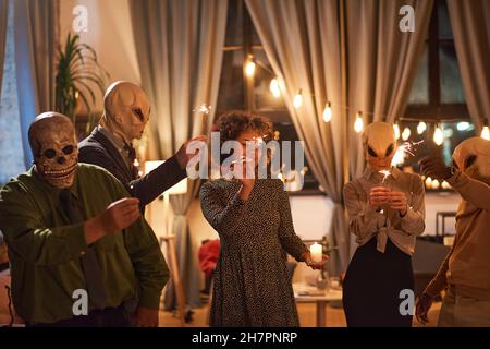 Gruppe von Menschen in unheimlichen Masken halten Wunderkerzen und tanzen während der Halloween-Party Stockfoto