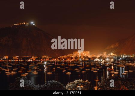 Eine Nachtaufnahme einer Bucht von Botafogo in Rio de Janeiro, Brasilien, mit vielen Segelbooten, die leicht auf dem Wasser schwanken, einem Berg Stockfoto