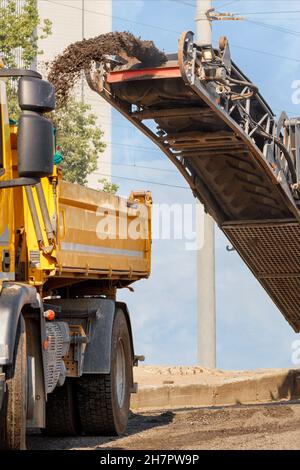 Ein Straßenrouter entfernt die obere Schicht alten Asphalts von einem Straßenabschnitt und lädt ihn auf einen Kipper. Stockfoto