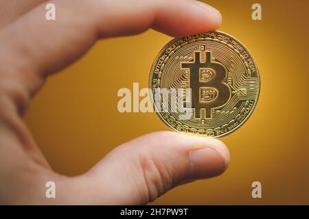 Galicien, Spanien - 20. November 2021: Hand mit einer Bitcoin-Münze auf gelbem Hintergrund. Stockfoto