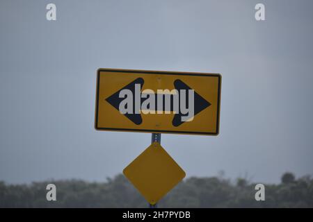 Schwarze Pfeile auf einem gelben Schild weisen darauf hin, dass der Verkehr abbiegen muss. Stockfoto