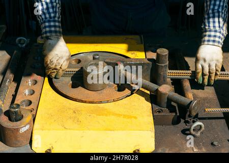 Hände eines Arbeiters bei der Arbeit an der Ankerbiegemaschine. Rebars mit Rebar Biegemaschine im Werk. Arbeiter mit Biegerebenmaschine für Reinf Stockfoto