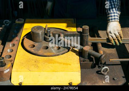 Hände eines Arbeiters bei der Arbeit an der Ankerbiegemaschine. Rebars mit Rebar Biegemaschine im Werk. Arbeiter mit Biegerebenmaschine für Reinf Stockfoto