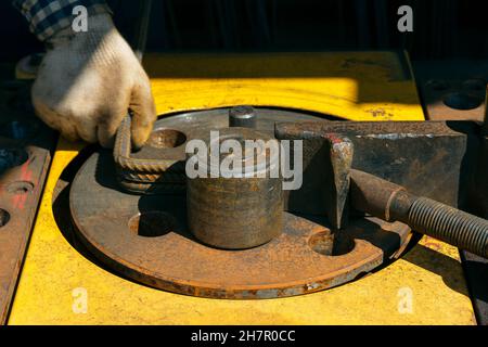 Hände eines Arbeiters bei der Arbeit an der Ankerbiegemaschine. Rebars mit Rebar Biegemaschine im Werk. Arbeiter mit Biegerebenmaschine für Reinf Stockfoto