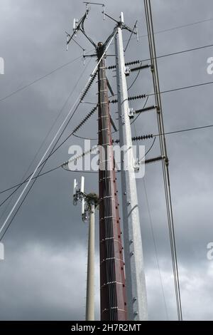 An einem trüben, bewölkten Tag kreuzen sich Hochspannungsleitungen mit Mobilfunkmasten. Stockfoto