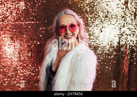 Stilvolle ältere Frau in weißem Pelzmantel trägt rosa Brillen Spaß im Studio Stockfoto