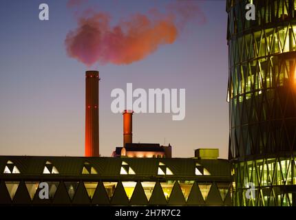 24. November 2021, Hessen, Frankfurt/Main: Im Abendlicht erscheint der Dampf eines Schornsteins des Kraft-Wärme-Koppwerks am Frankfurter Westhafen, das mit Kohle betrieben wird und Strom und Fernwärme für viele Wohnungen der Stadt bereitstellt, orange und rosa. Foto: Frank Rumpenhorst/dpa Stockfoto
