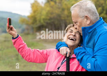 Glückliches Senior-Paar, das Spaß hat, ein Selfie während des Trekkingtages im Wald zu machen - Fokus auf das Gesicht der Frau Stockfoto