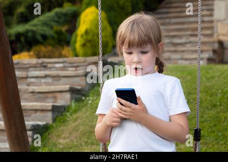 Überrascht Mädchen im Grundschulalter, jung schockiert überrascht Kind hielt ihr Smartphone in den Händen, Blick auf ihr Handy. Porträt, Nahaufnahme, c Stockfoto