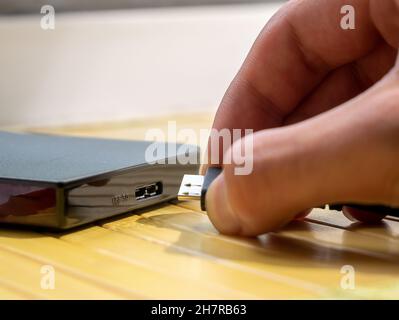 USB type 3.0 HDD, man inserting a cable into a portable external hard drive, object detail, hand extreme closeup. Digital data, personal media storage Stockfoto
