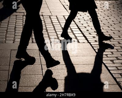 Zwei anonyme, unkenntlich gewordenen Menschen, die durch die Straße gehen, dunkelschwarze Beinumrisse, Schatten. Fußgänger im Freien, Gesellschaft, Anonymität, Lonelin Stockfoto