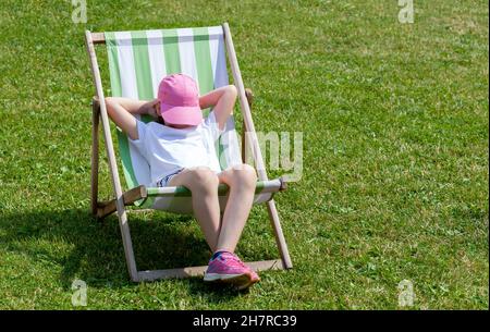 Junge Grundschulkinder, Mädchen, die auf einer Sonnenliege liegen, sich entspannen, schlafen, ein Nickerchen im Garten allein machen. Freizeit, Sommerferien r Stockfoto