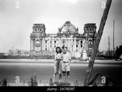 Im August 1947 besuchte der RAF-Pilot Browne Berlin und nahm eine Begleiterin mit auf eine Sightseeing-Tour durch die Stadt. Hier stehen sie vor den Ruinen des Reichstags. Das Mädchen ist unbekannt, möglicherweise eine Kellnerin, die an ihrer Schürze vorbei geht. P/O Browne flog am 12th. August 1947 nach Berlin Gatow und am 19th. August 1947 nach RAF Bückeberg. Stockfoto