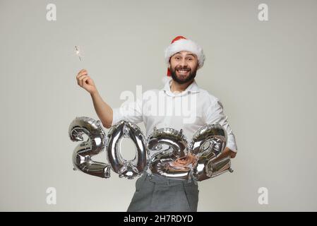 Ein lächelnder Mann in einem roten Samthut hält mit einer Hand silberne Luftballons in der Form von 2022 und mit der anderen Hand einen Funker. Ein Typ mit einem Stockfoto