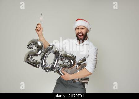 Ein lächelnder Mann in einem roten Samthut hält mit einer Hand silberne Luftballons in der Form von 2022 und mit der anderen Hand einen Funker. Ein Typ mit einem Stockfoto